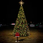 50-foot commercial Christmas panel tree with warm white lights and red ornaments installed outdoors at night