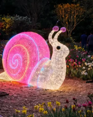 Glowing snail sculpture in flower garden at night