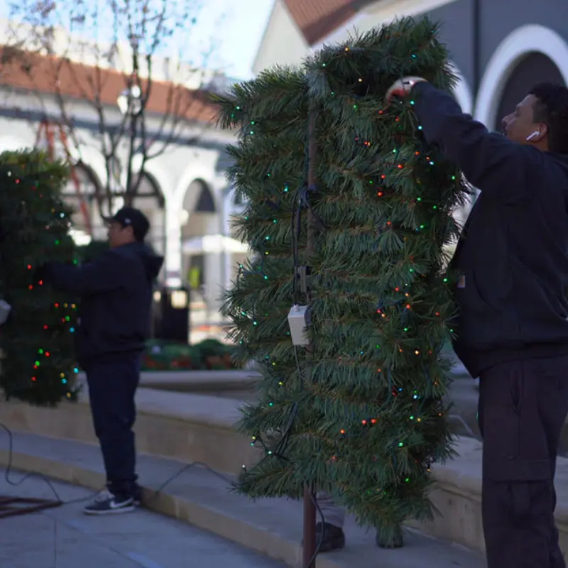 Workers installing lit Christmas wreaths outdoors