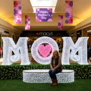 Woman sitting before illuminated MOM Mother's Day commercial dimensional display