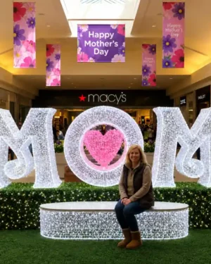 Woman sitting before illuminated MOM Mother's Day commercial dimensional display