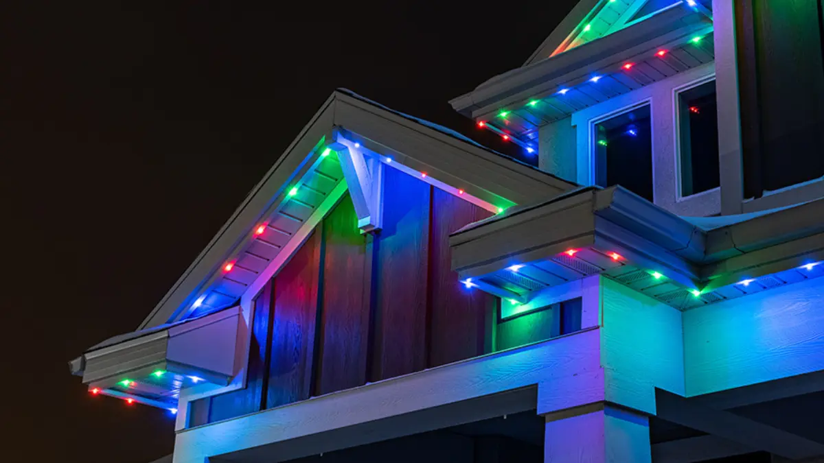 Colorful holiday lights illuminate house eaves at night